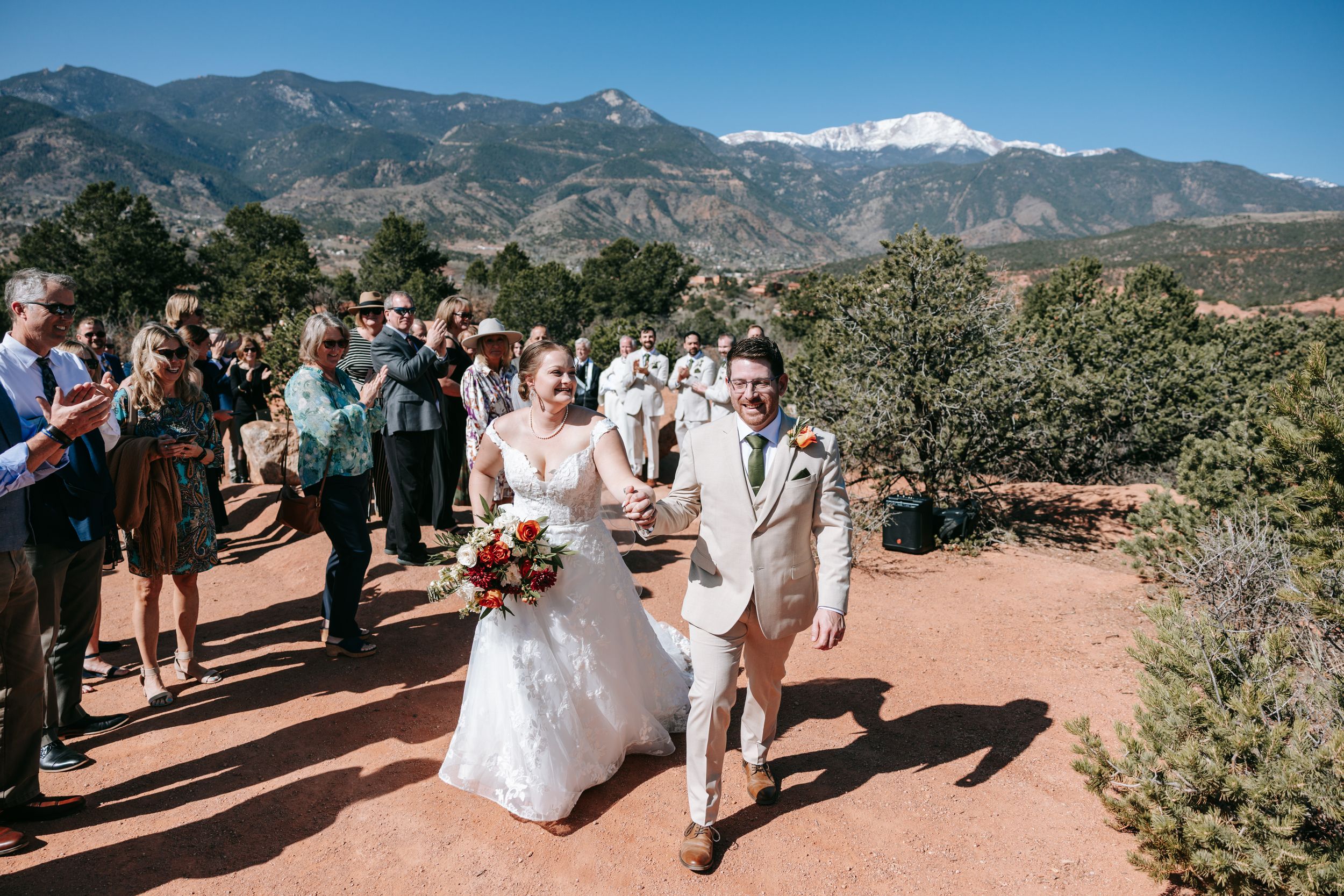 A scenic mountain landscape serves as the backdrop for an outdoor wedding ceremony in rugged terrain.