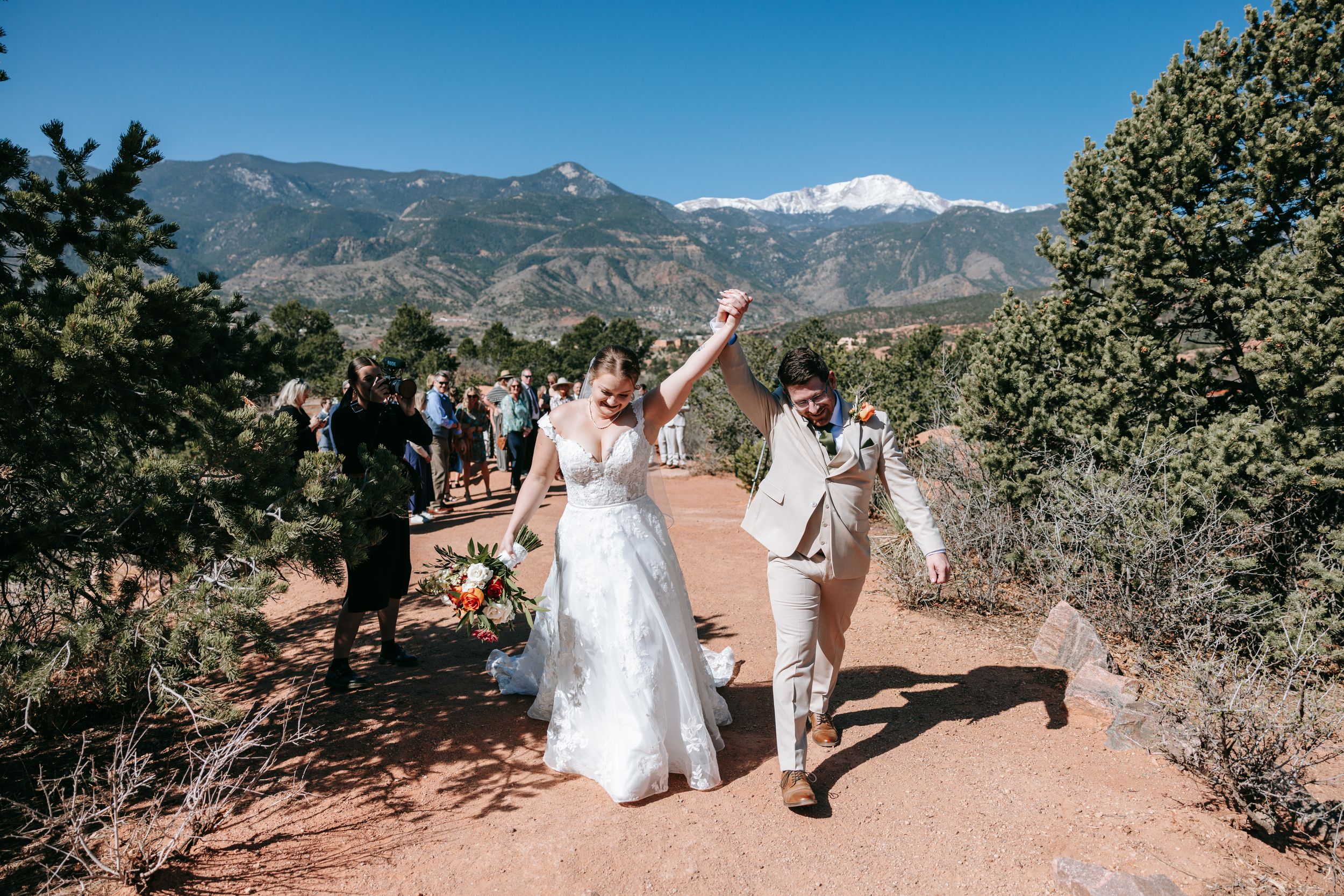 A panoramic view of snow-capped mountains and rolling hills with wedding guests gathered on a scenic outdoor path.