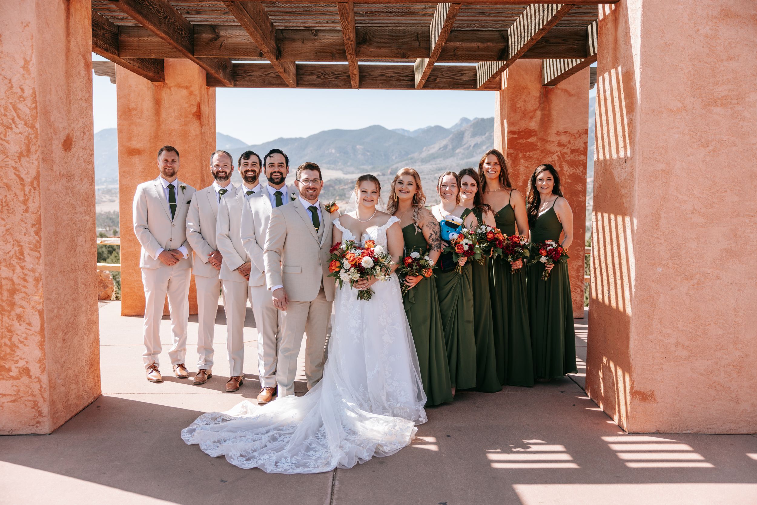 Wedding party poses for formal photos in a rustic terracotta colored courtyard setting.