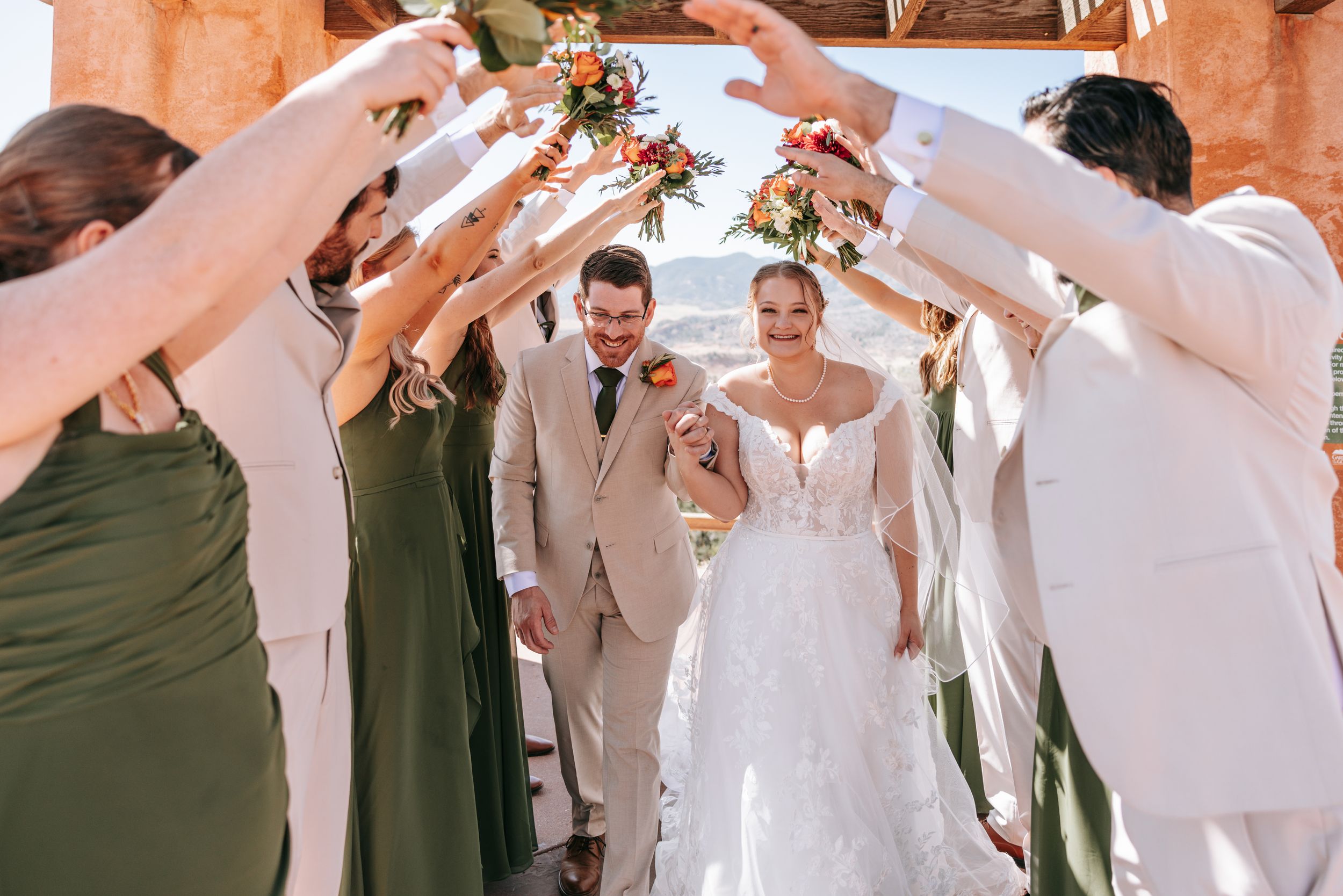 Wedding party performs traditional sword arch ceremony on red rock pathway with mountain views.