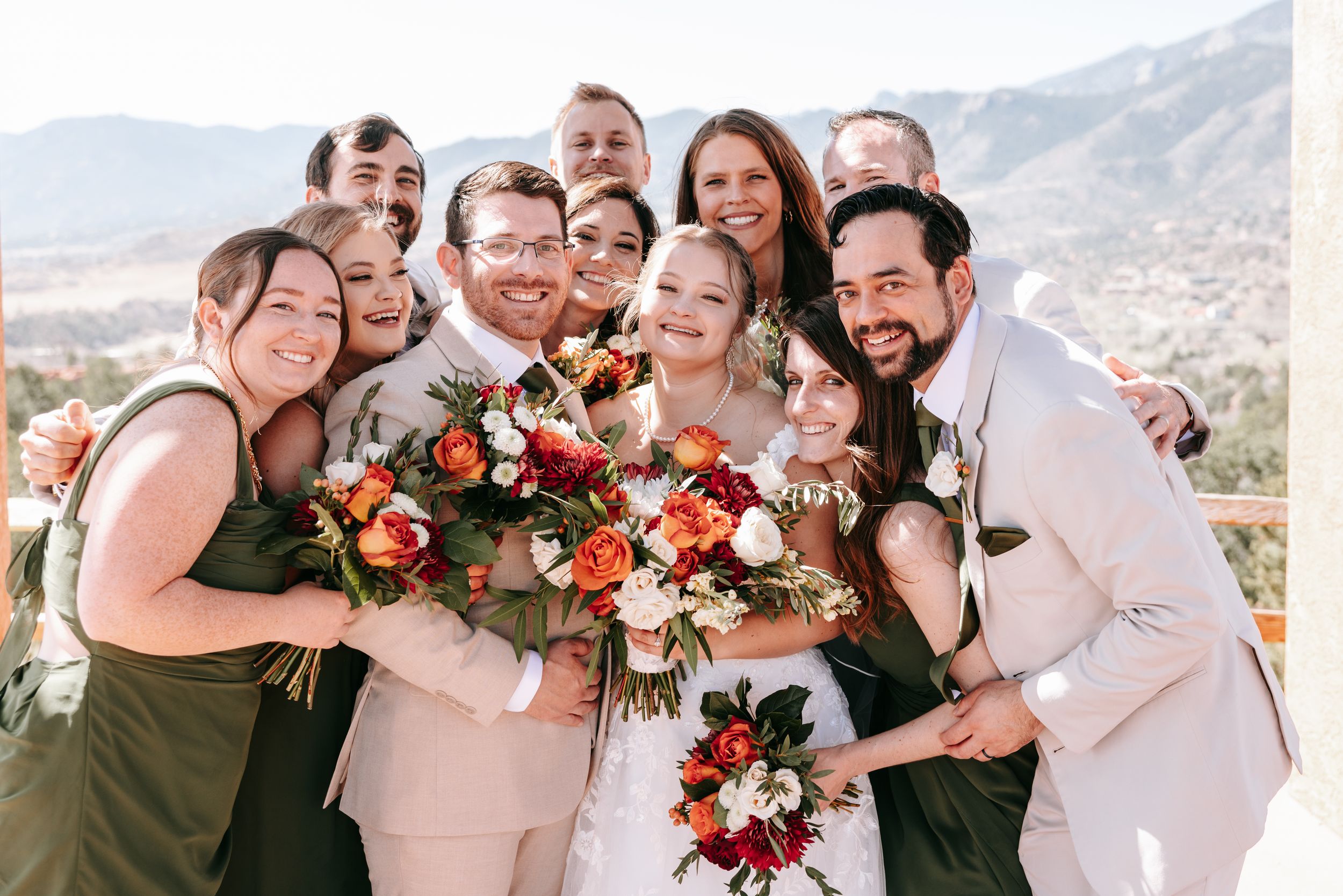 A wedding party poses together with colorful autumn bouquets against a mountain backdrop.