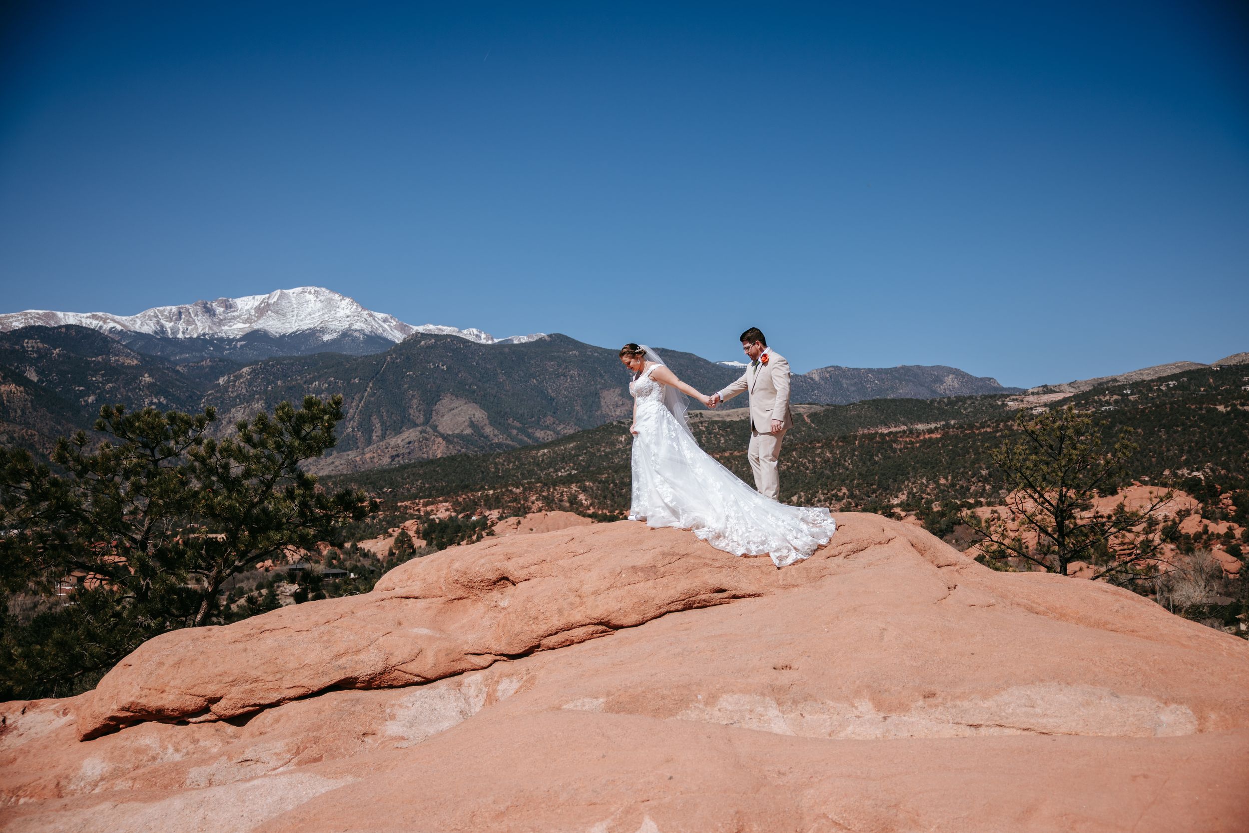 A romantic wedding photo on red rocks at Garden of the Gods with snow-capped Pikes Peak mountain in background.
