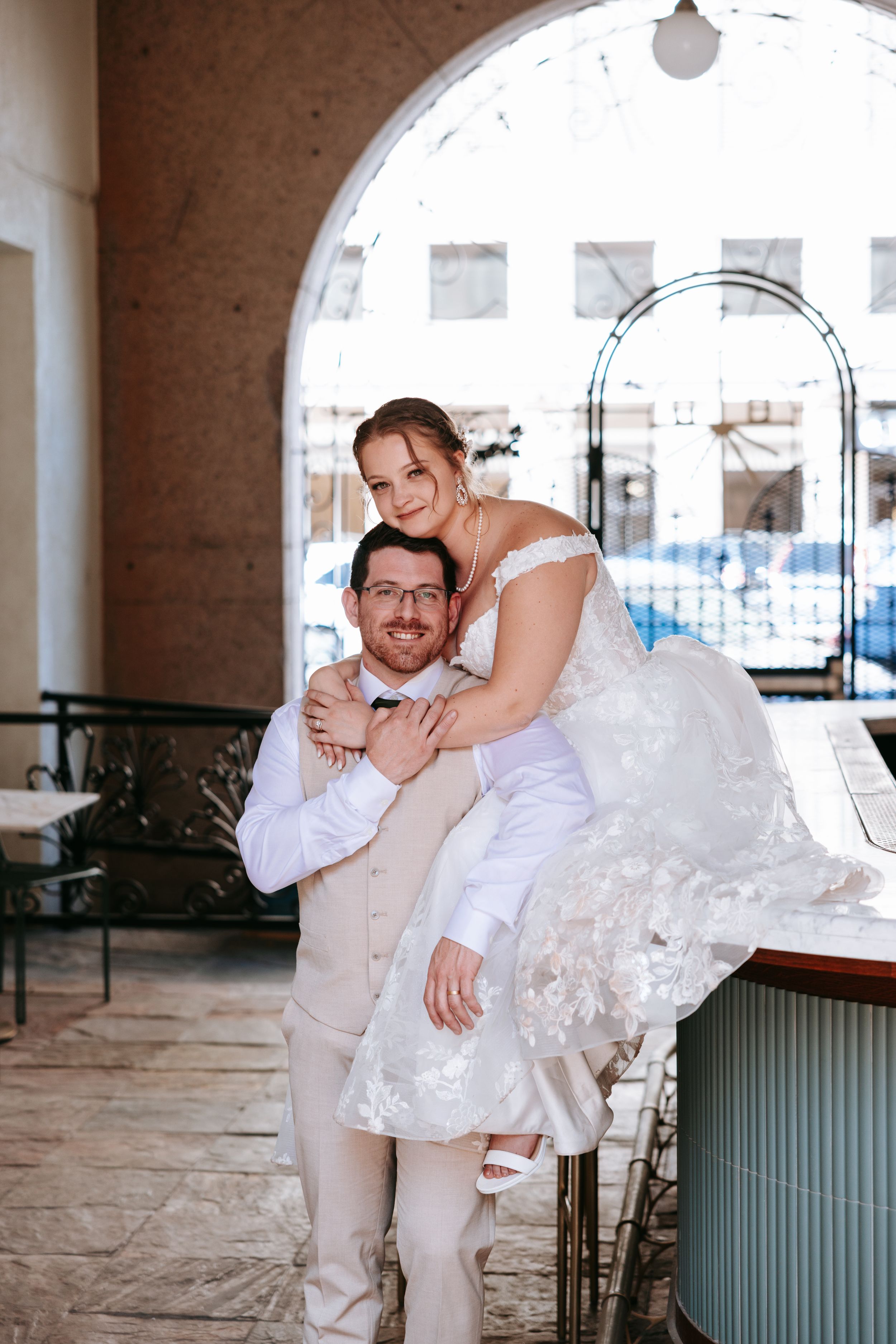 A romantic wedding photo shows a couple embracing under an arched walkway, with the bride wearing a lace gown.