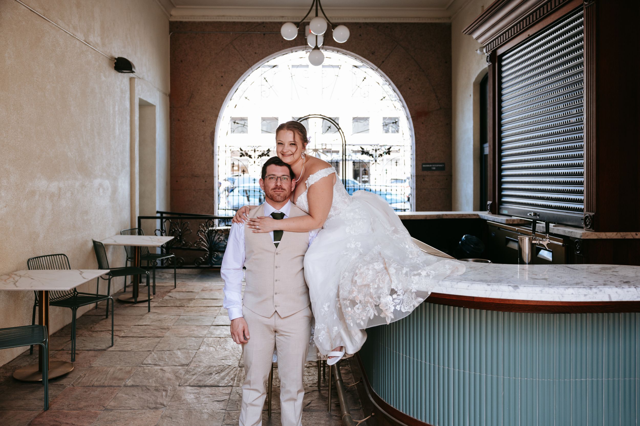A newlywed couple poses together in an arched passageway with turquoise counter and dining area.