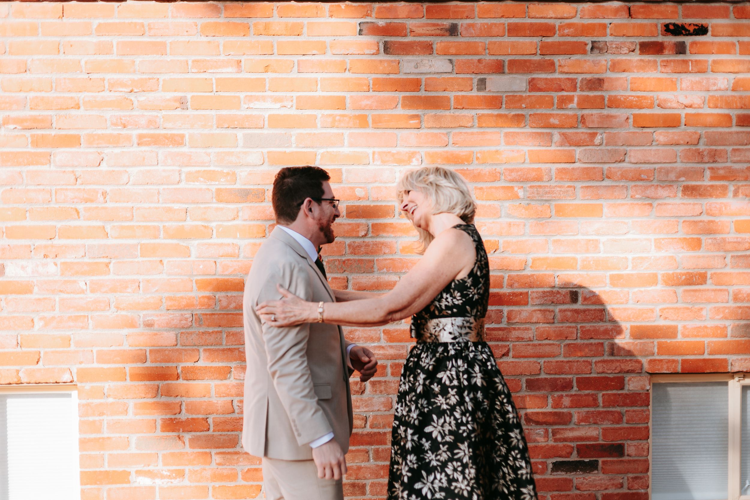 A couple shares an intimate moment against a rustic brick wall background in natural lighting.
