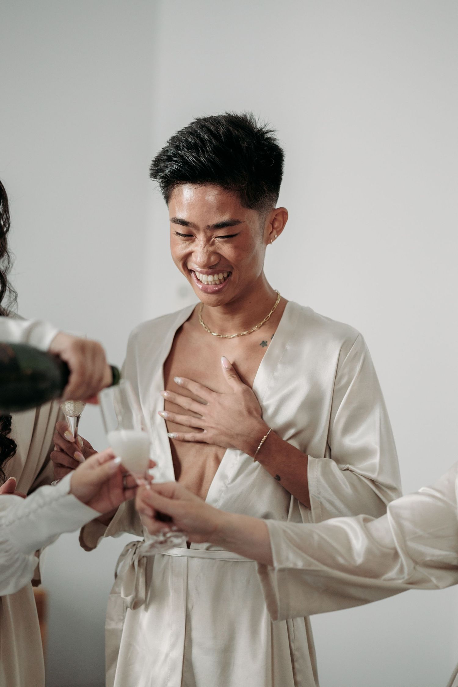 A smiling person wearing a cream silk robe laughs while drinking champagne. Captured by Montreal wedding photographer, Aliza Dworkind.