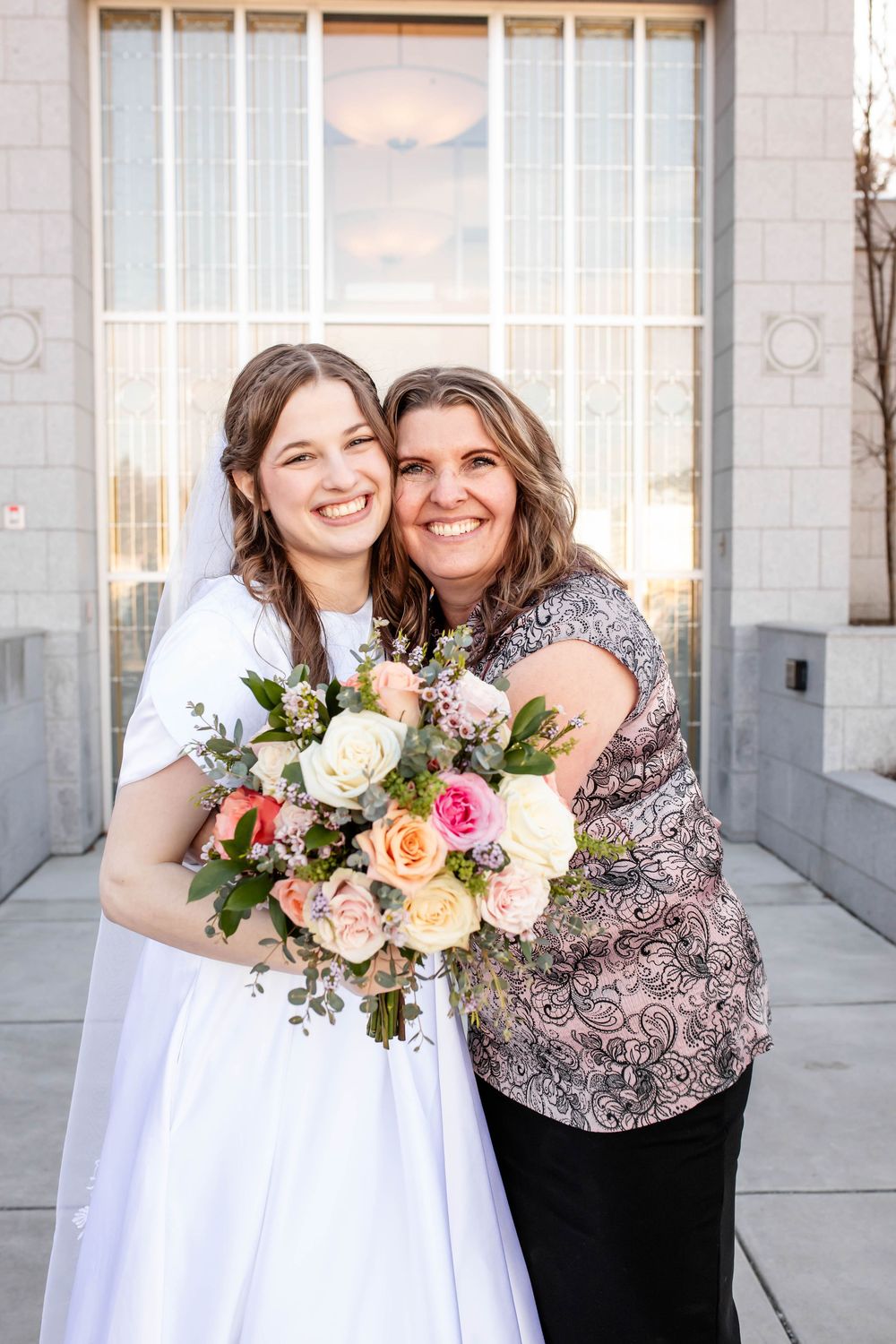 Two people sharing a tender moment with floral bouquets outside a temple on a wedding day.