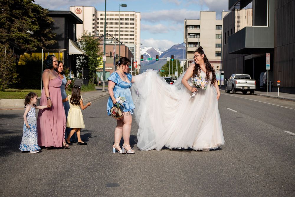 Wedding party poses on a city street with tall buildings and mountains visible in the background.