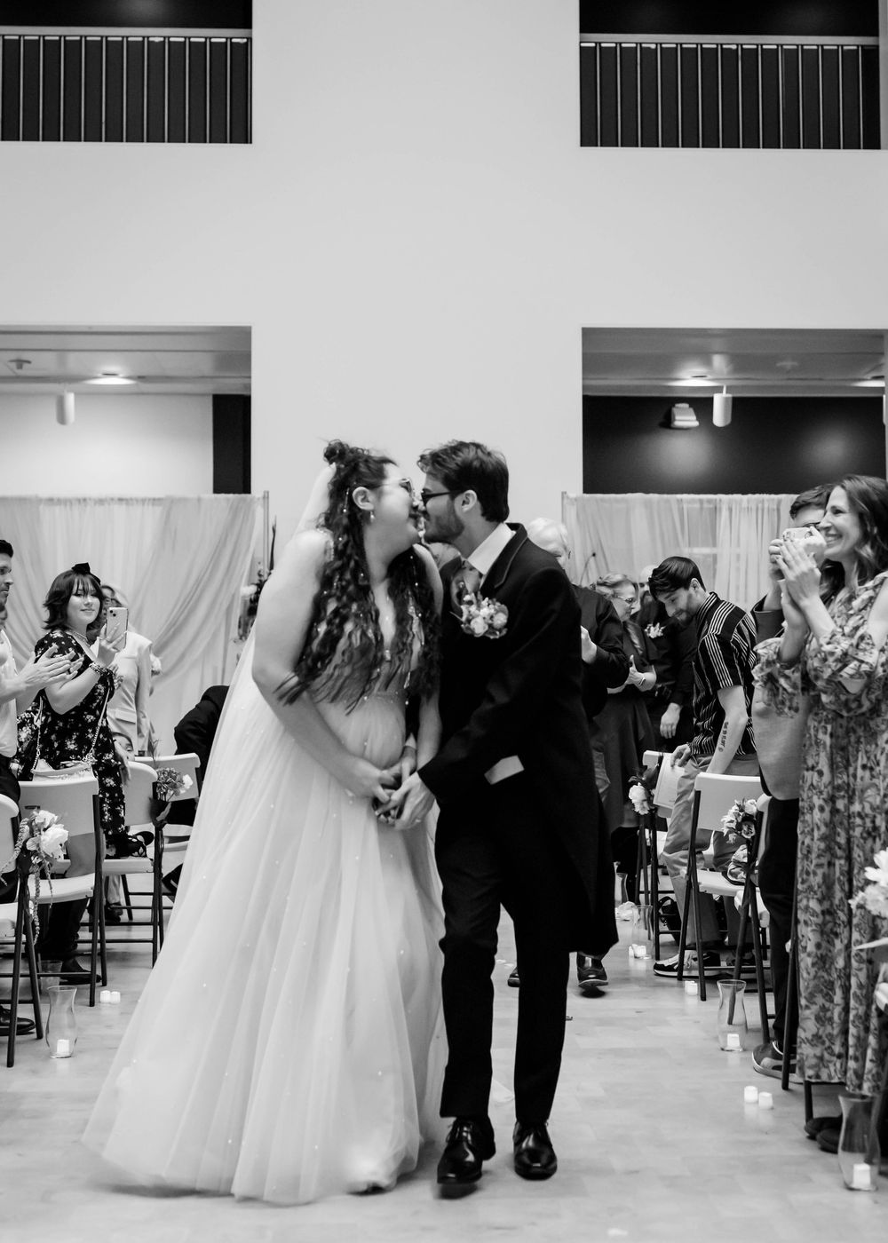 People in formal attire dance together during what appears to be a wedding reception in a white-walled ballroom.