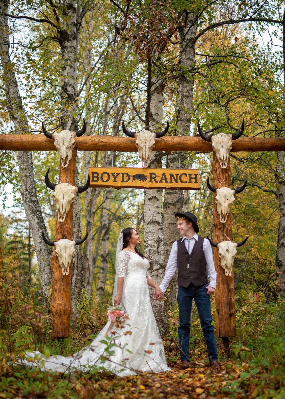 Western autumn wedding at Boyd Ranch with couple standing under rustic wooden arch decorated with cattle skulls.