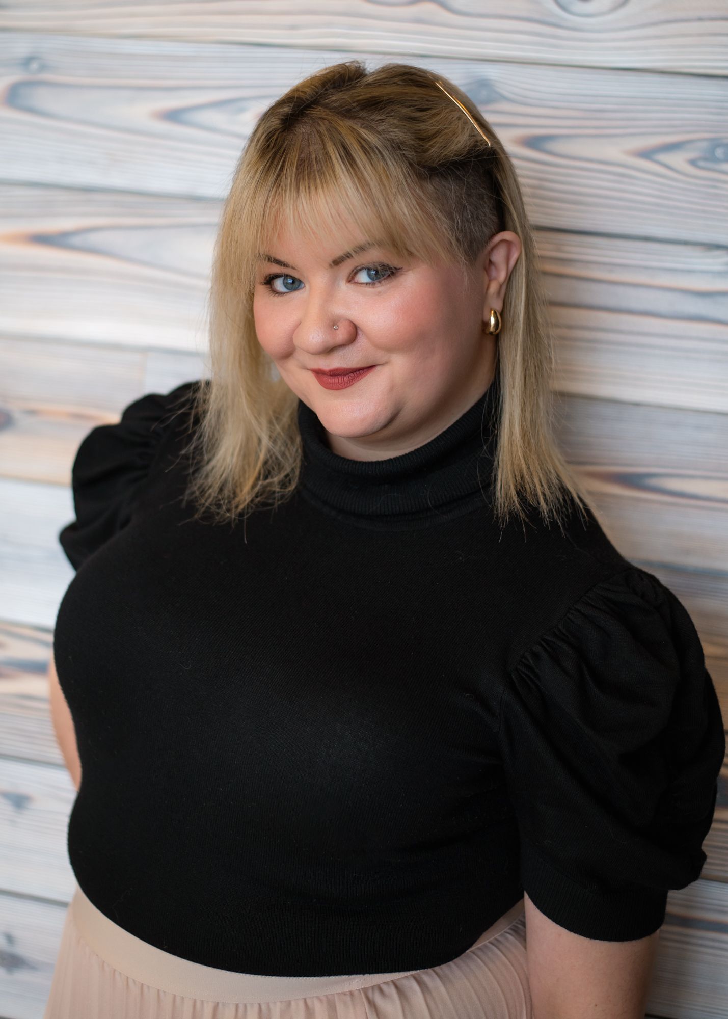 Casual portrait against textured wall showing bright smile wearing olive button-down shirt over white t-shirt.