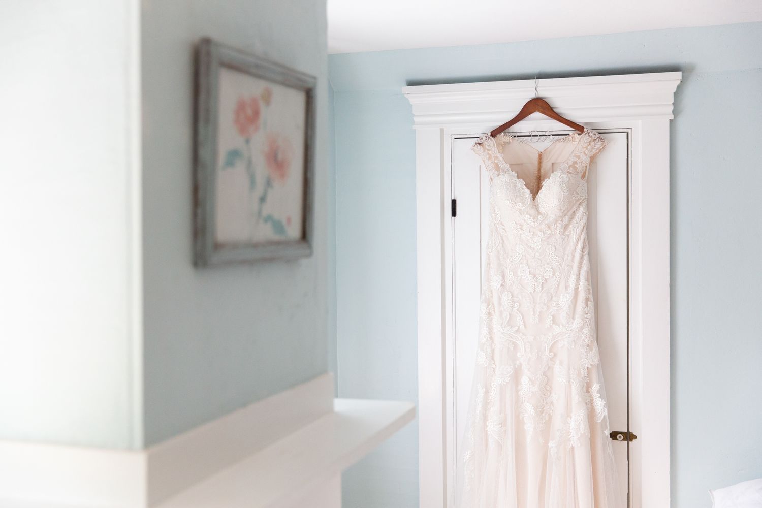 White wedding dress hanging in a light blue room with delicate details and natural lighting.