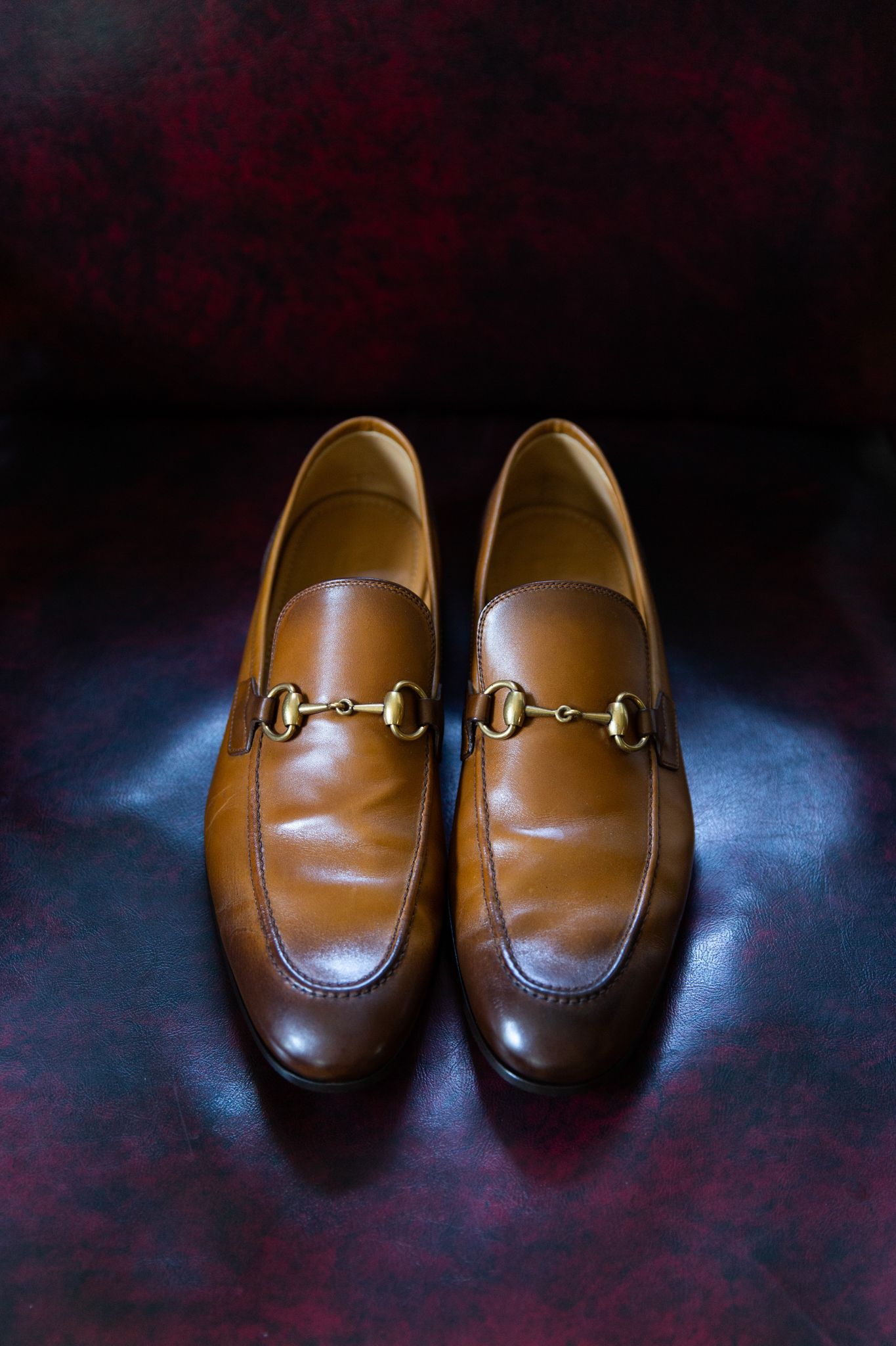 Brown leather Gucci loafers with gold horsebit detail photographed on dark surface.