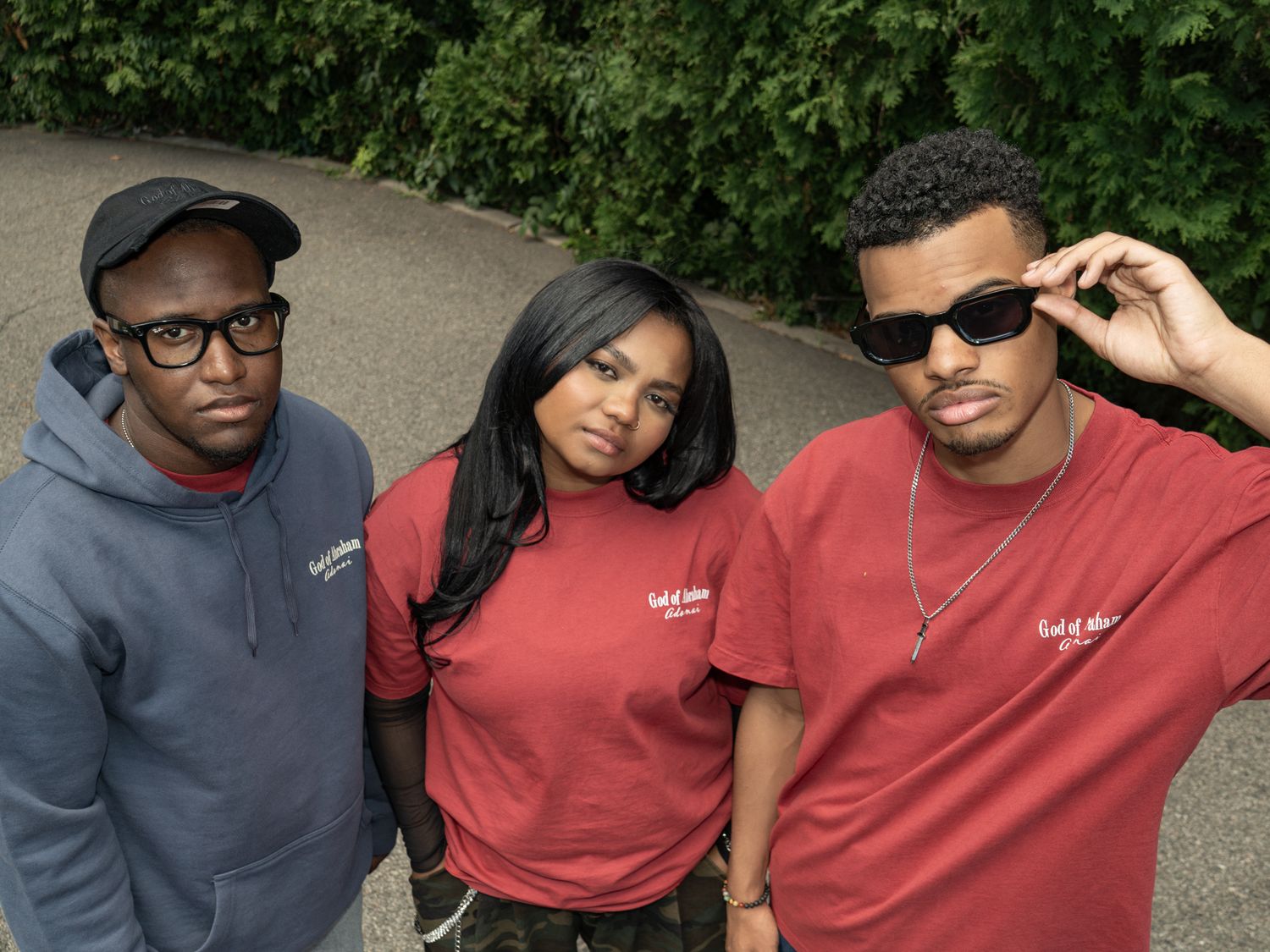 Three young adults wearing matching red branded t-shirts pose outdoors on a path surrounded by green trees.