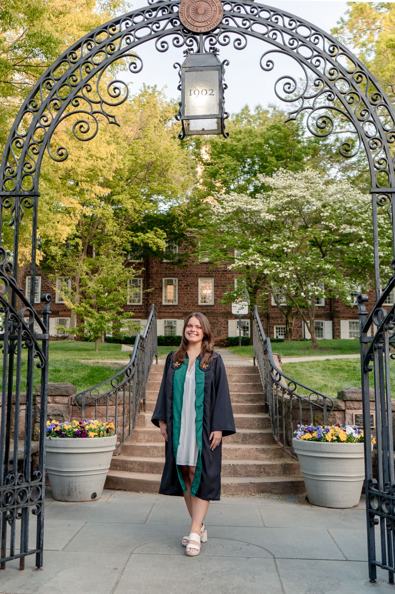 A sequence of graduation portraits under a decorative iron archway on a college campus.