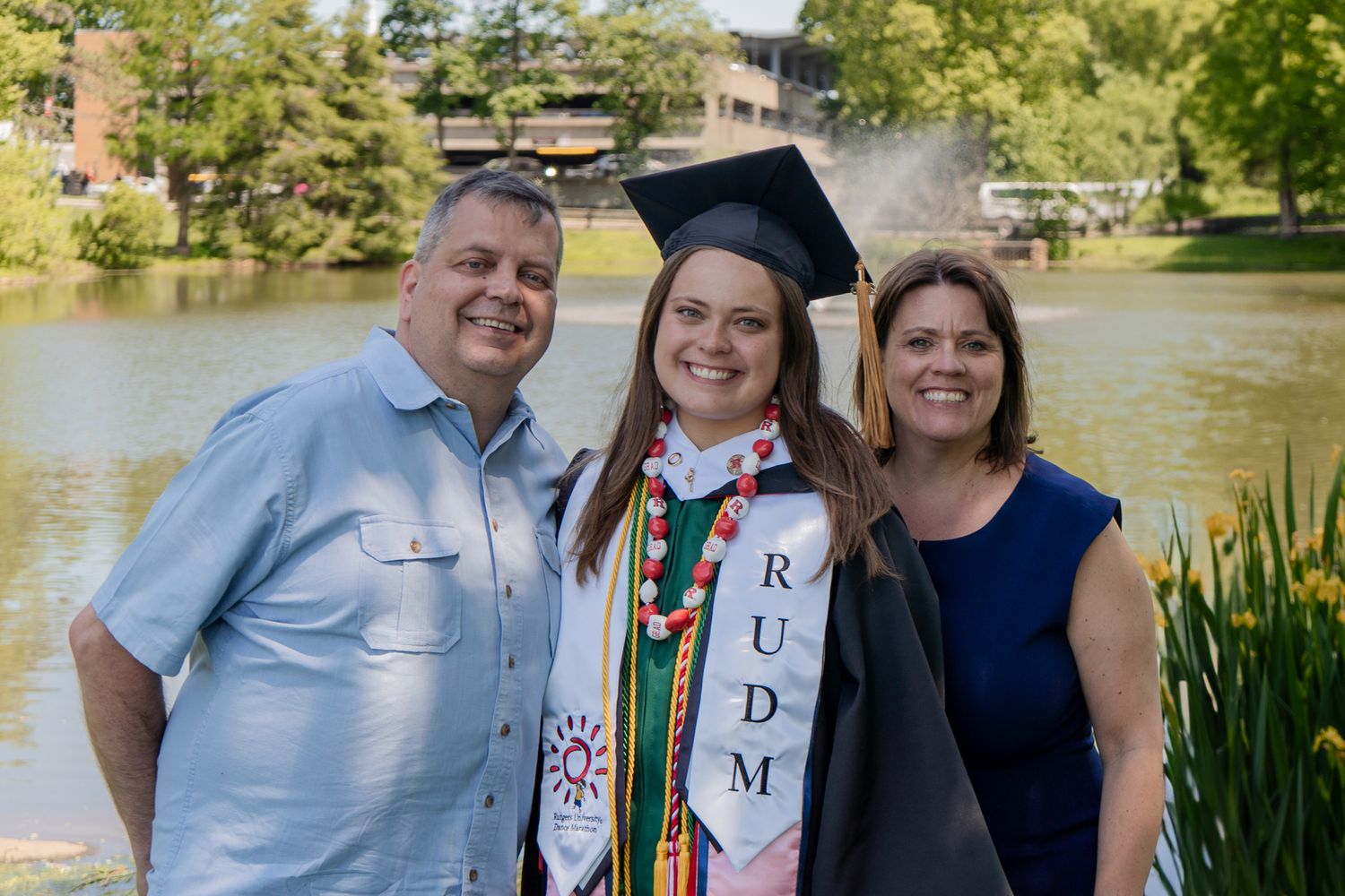 Graduates in formal attire pose with decorated stoles outdoors.