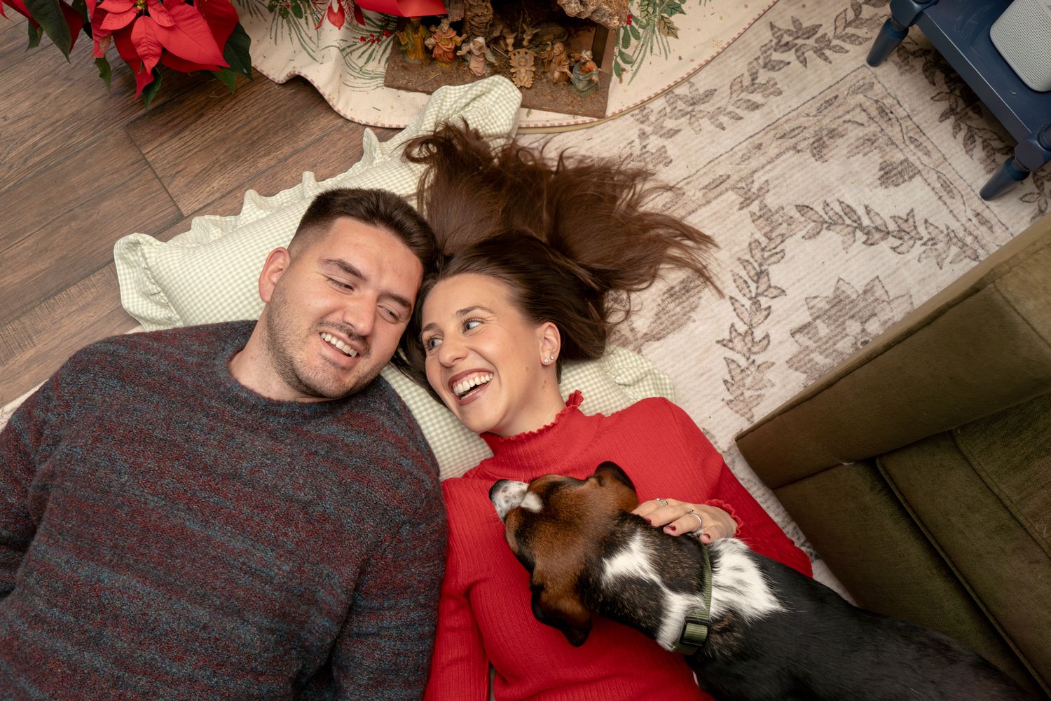 A couple in matching red sweaters cuddles together on a couch in a romantic holiday scene.