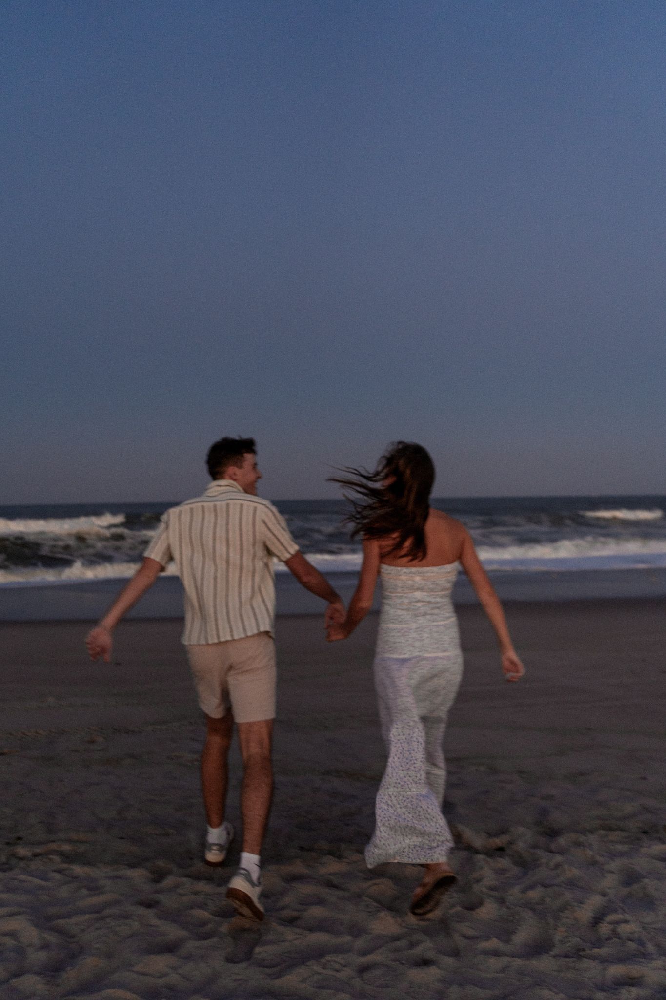 A couple running hand in hand on a beach at dusk.