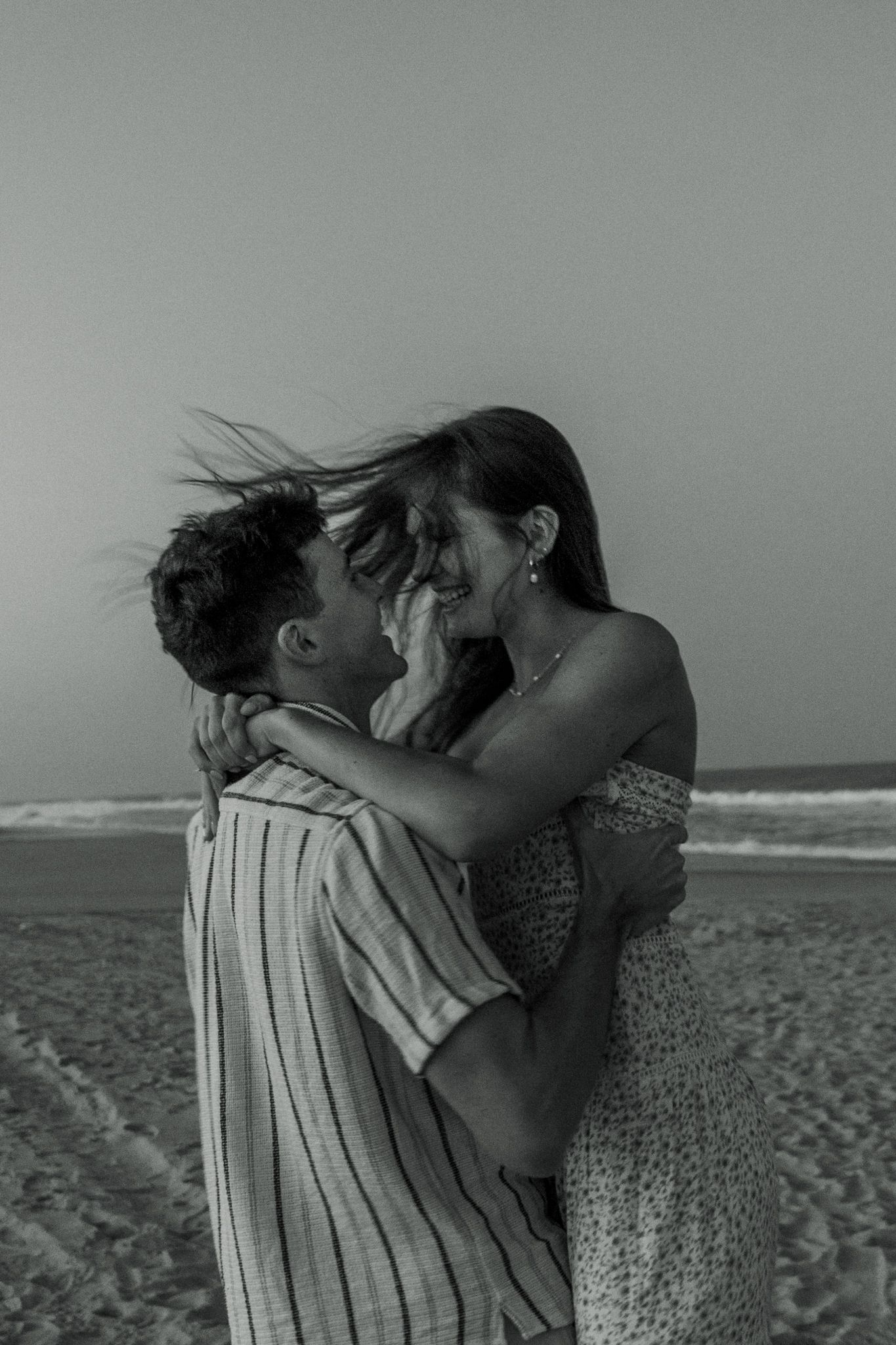 An intimate black and white portrait of a couple sharing a passionate moment on the beach.