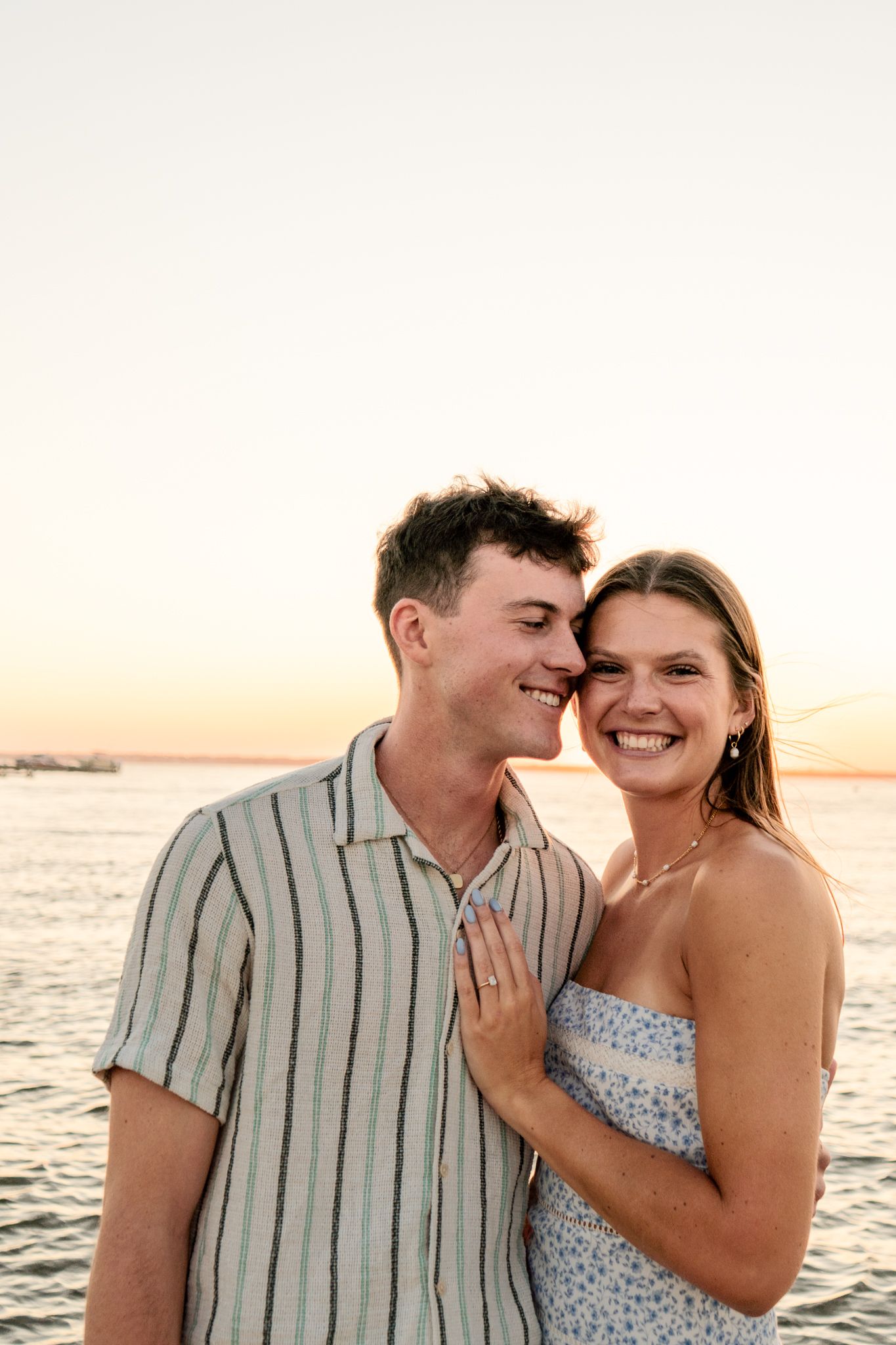 A joyful sunset portrait by the water with coastal homes in the background.