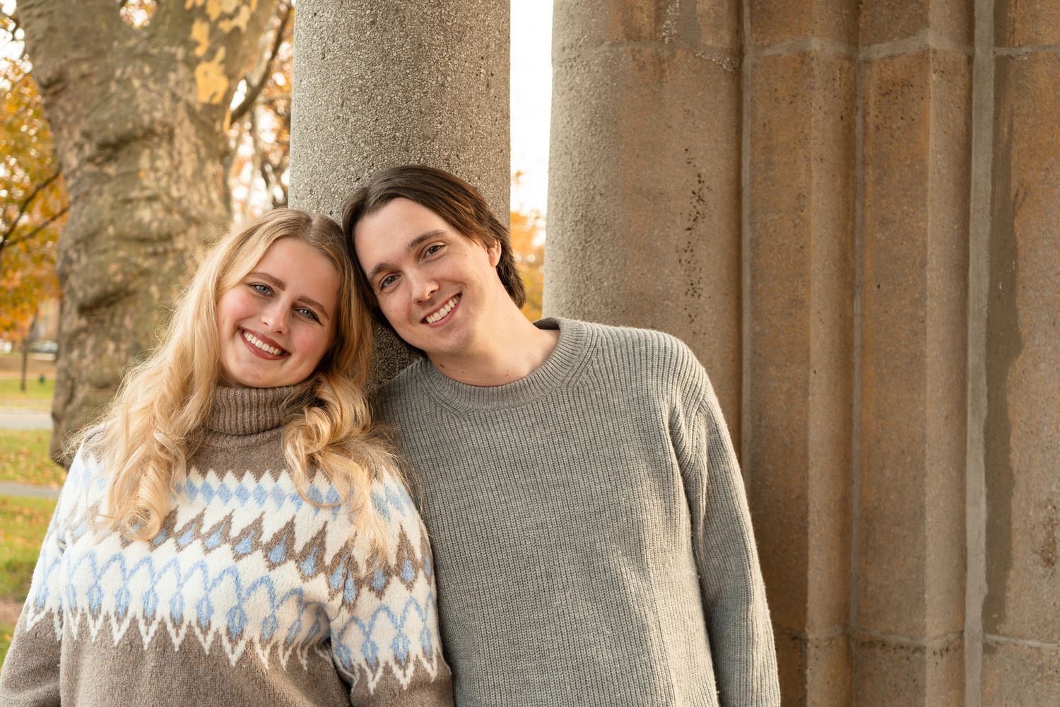 Casual engagement photos captured against stone architectural columns in warm autumn light.