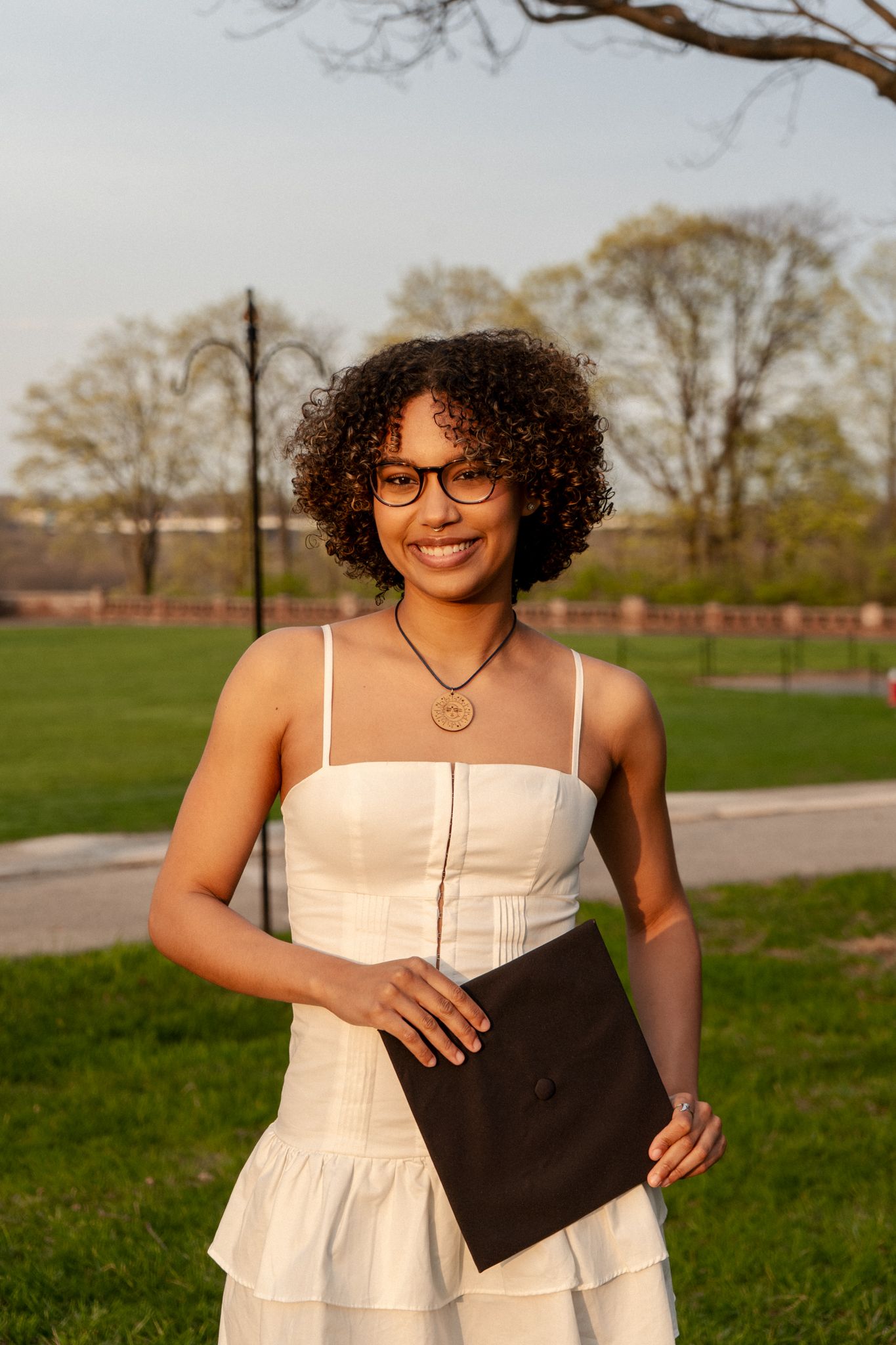 A series of outdoor graduation portraits featuring a white dress and black portfolio.