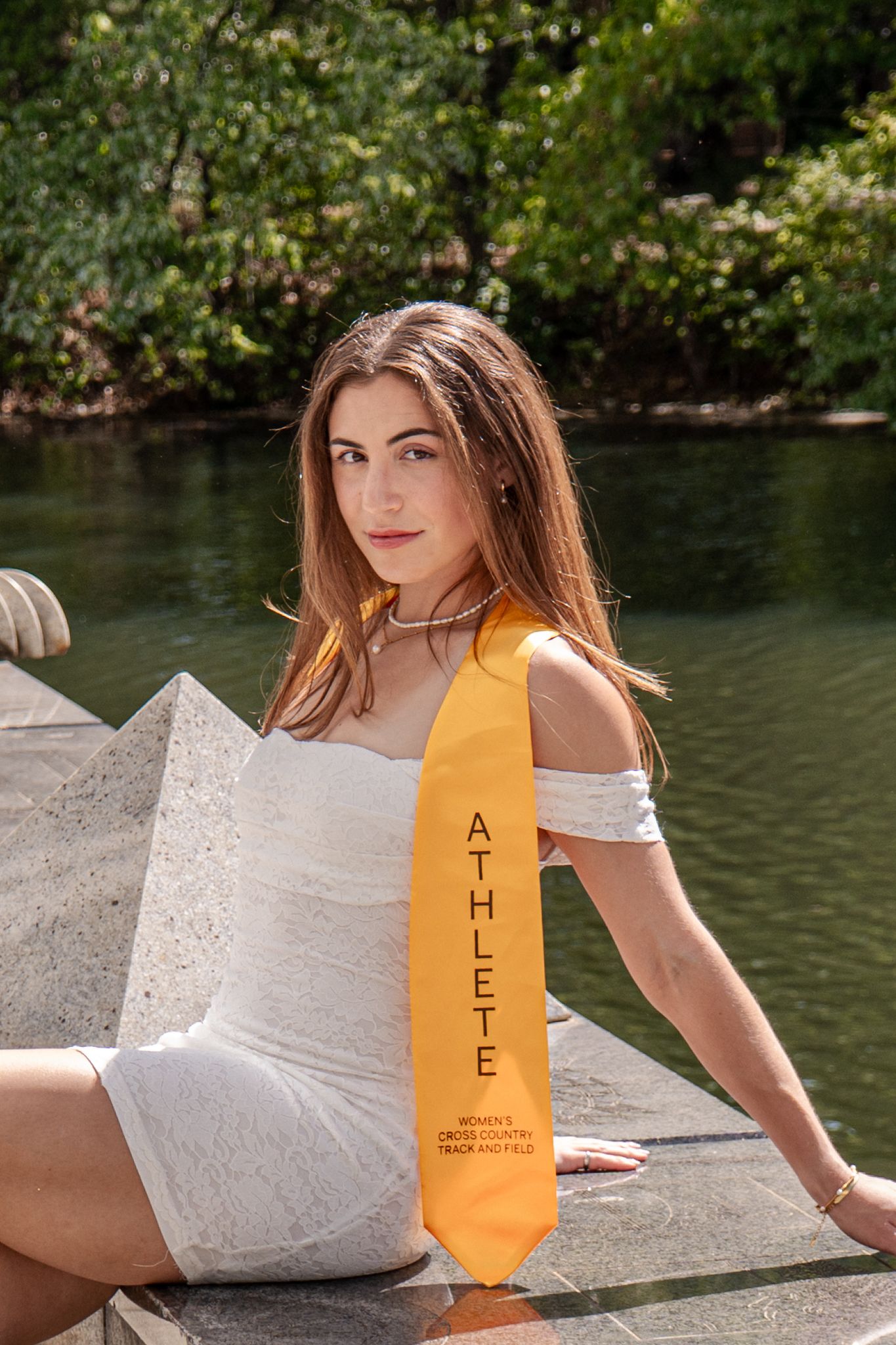 White lace dress and yellow graduation sash shown against waterfront background.