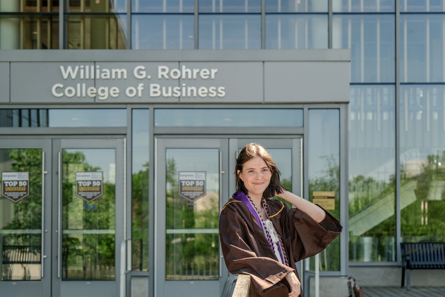 Graduate poses outside William G. Rohrer College of Business building.
