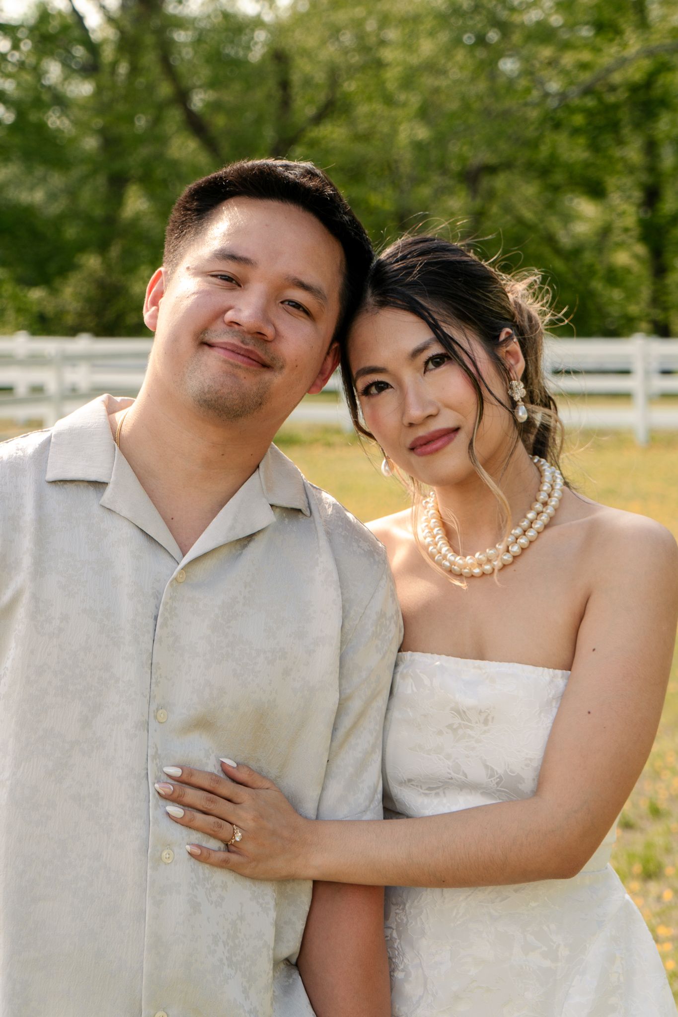 Couple in formal white attire embrace during outdoor photo session.