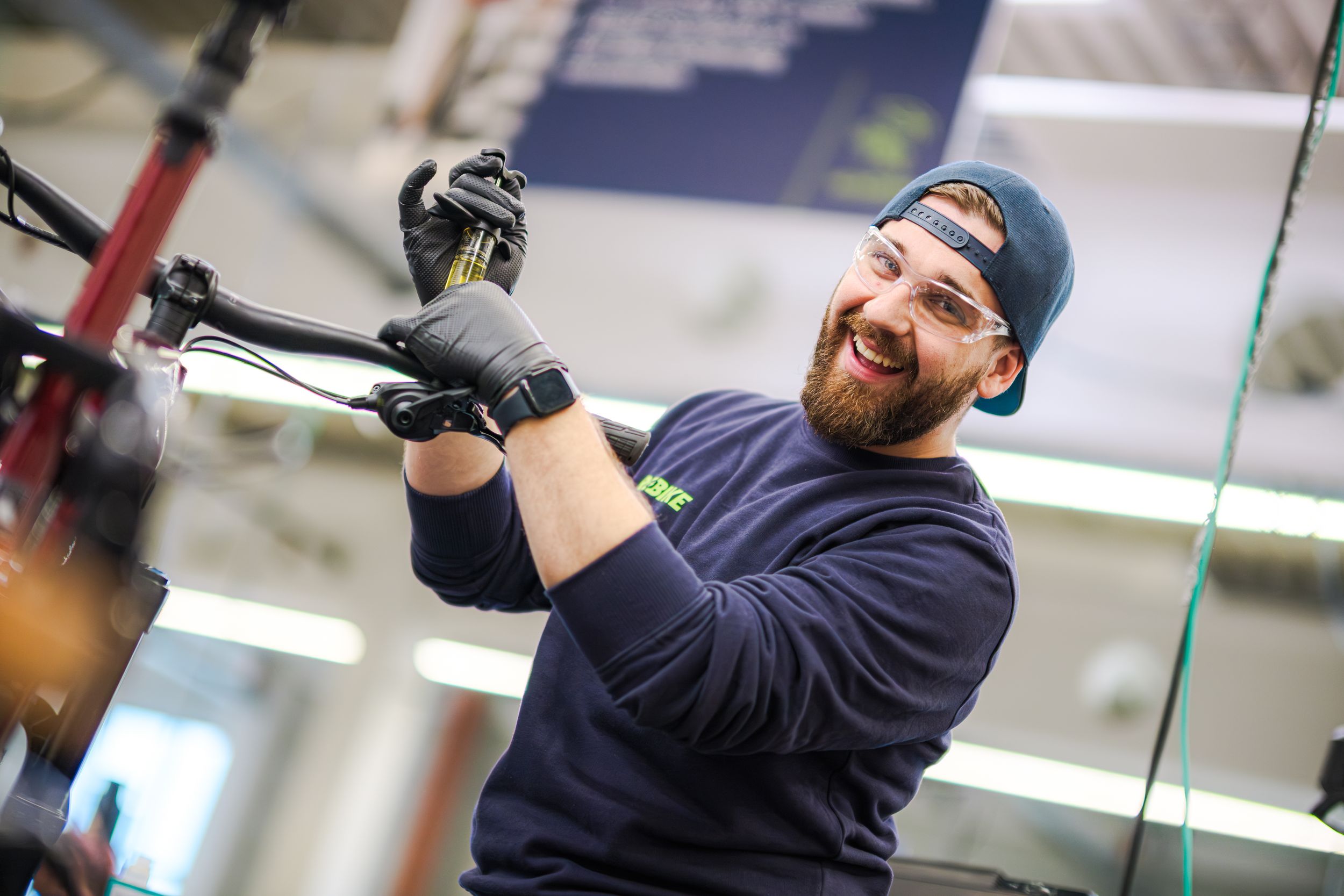 A bicycle mechanic in a navy cap and uniform takes practice swings in an indoor batting cage facility.