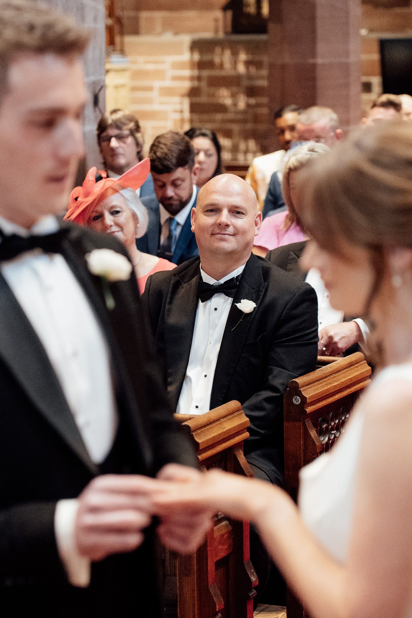 A formal church wedding scene where attendees in tuxedos look at their programs during a ceremony.