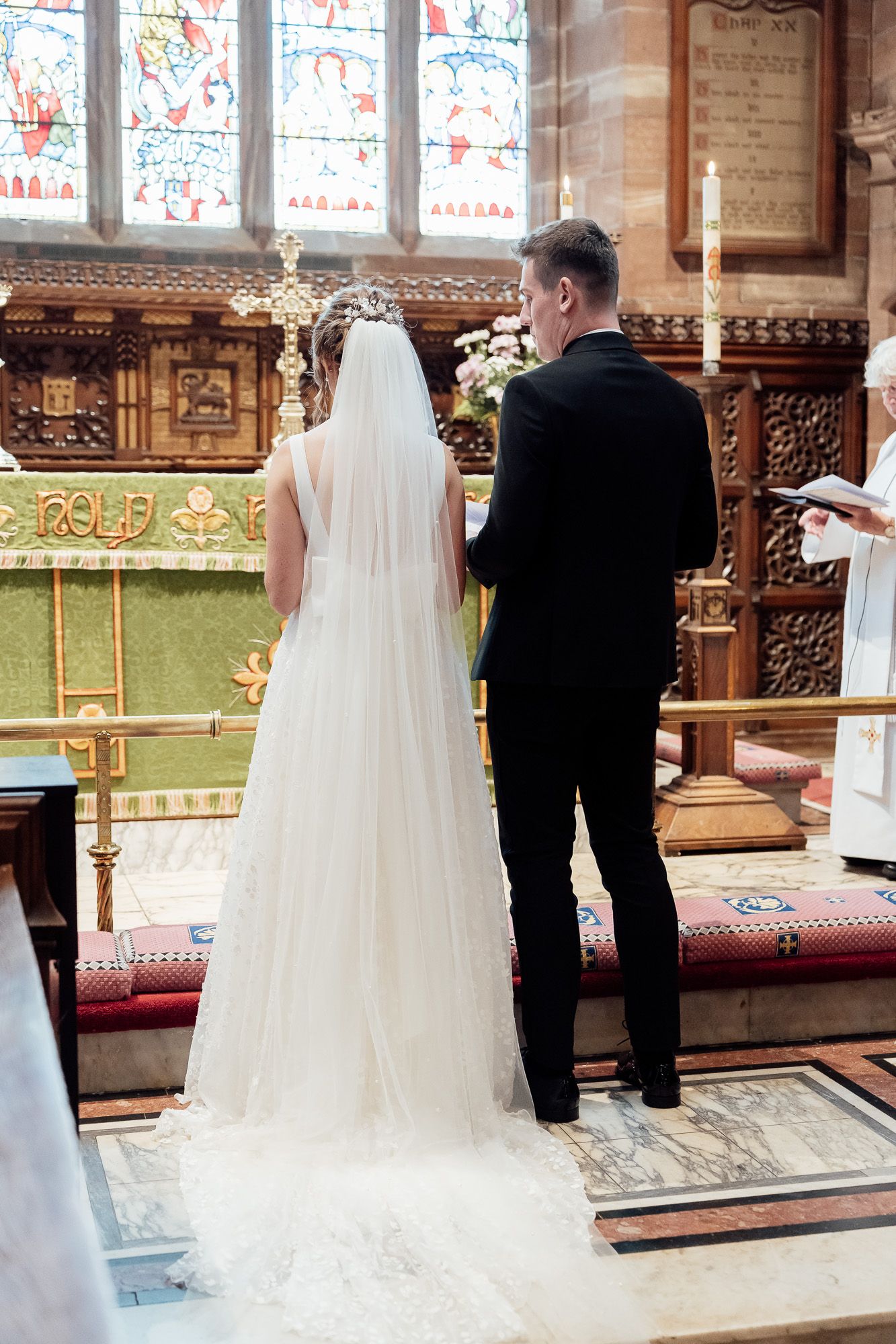 A wedding ceremony inside an ornate church with stained glass windows and carved wooden details, featuring a bride in white veil.