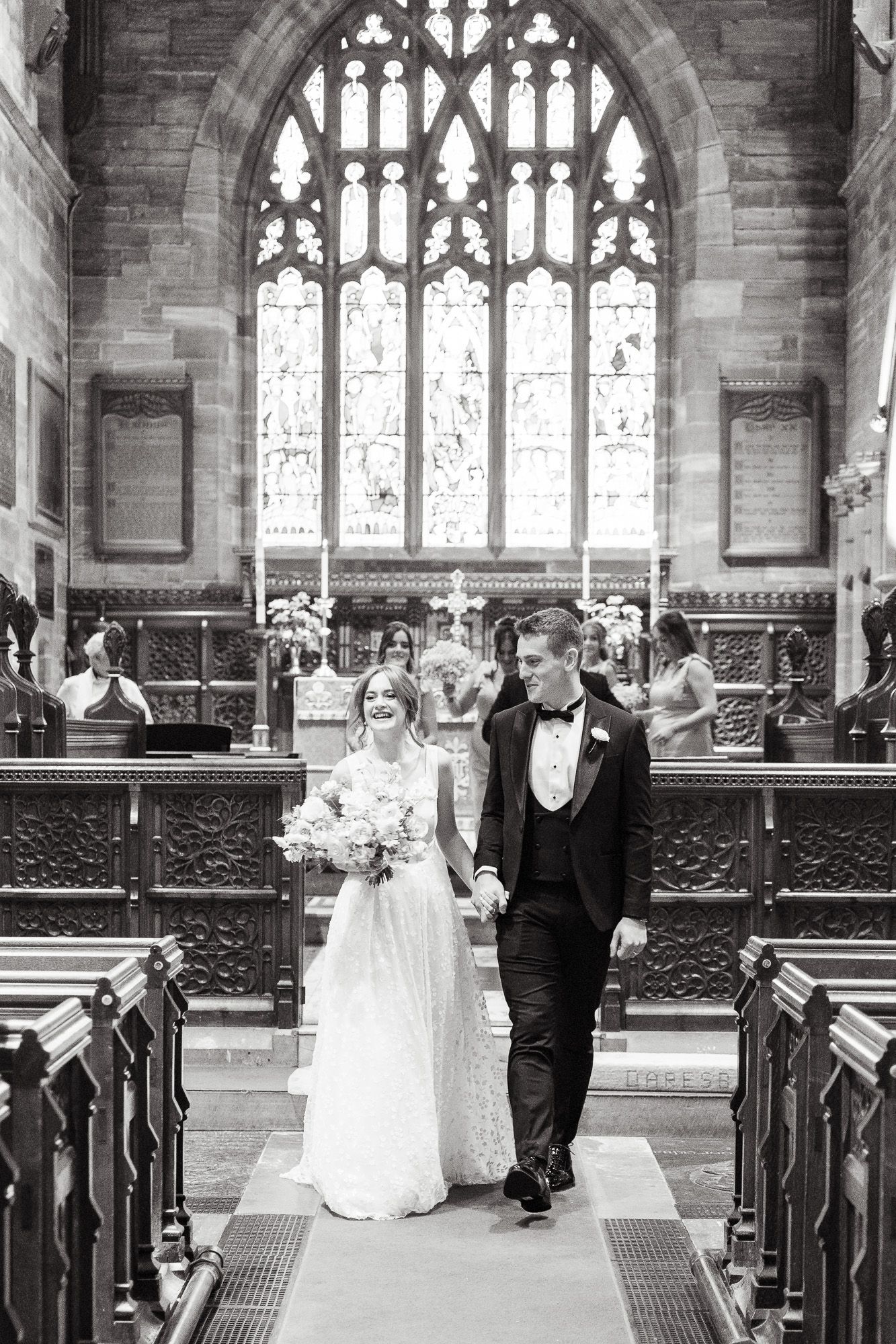 A wedding couple walks down the church aisle in a sequence of five black and white photographs.