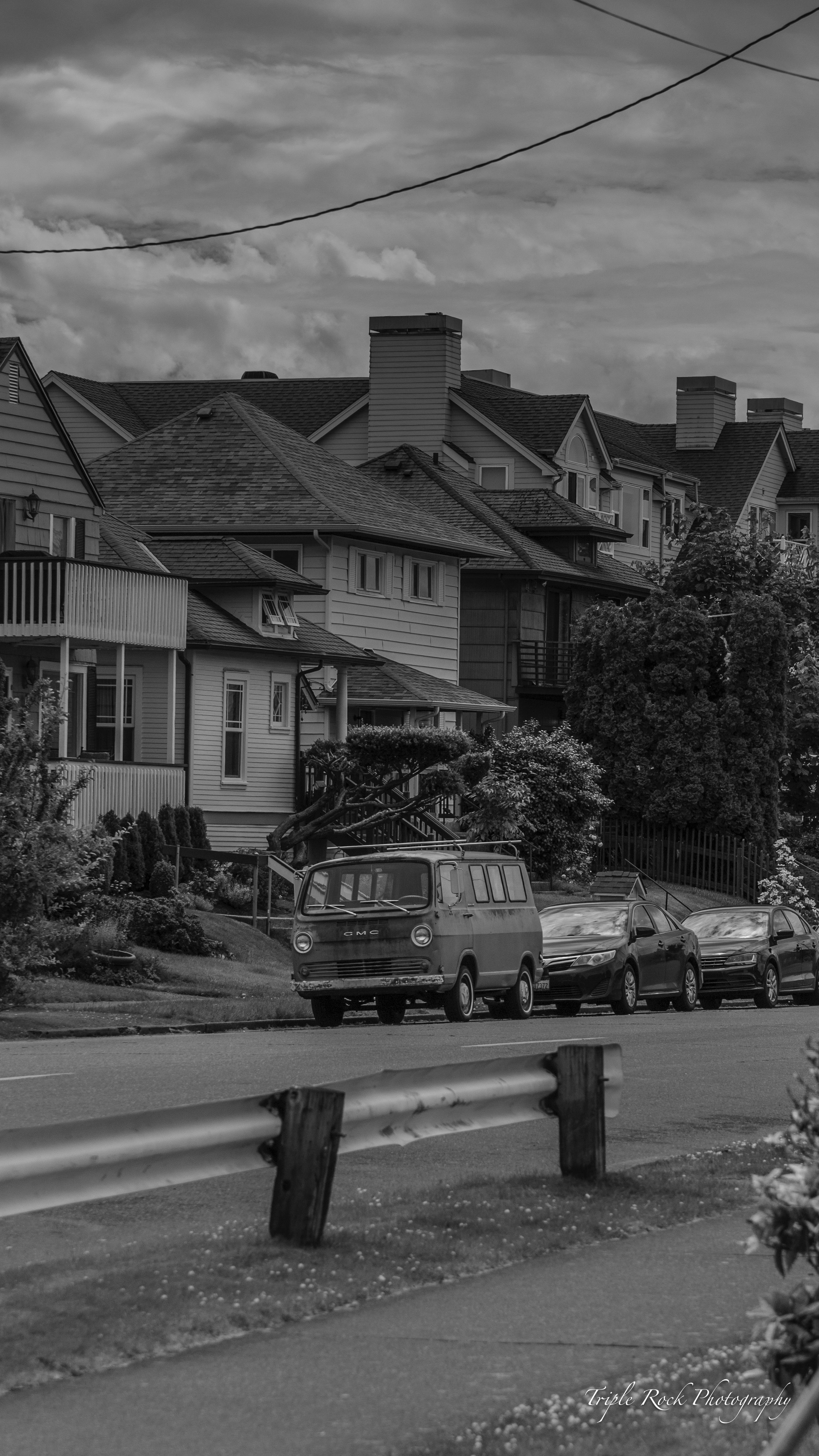 Black and white street scene with classic VW van parked among historic houses on a hillside.