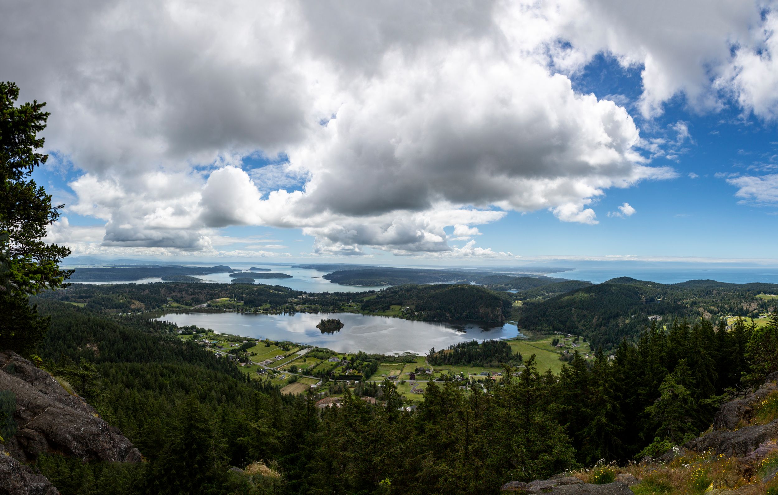 Panoramic mountain vista with dramatic cloudy skies over a green valley and distant peaks.