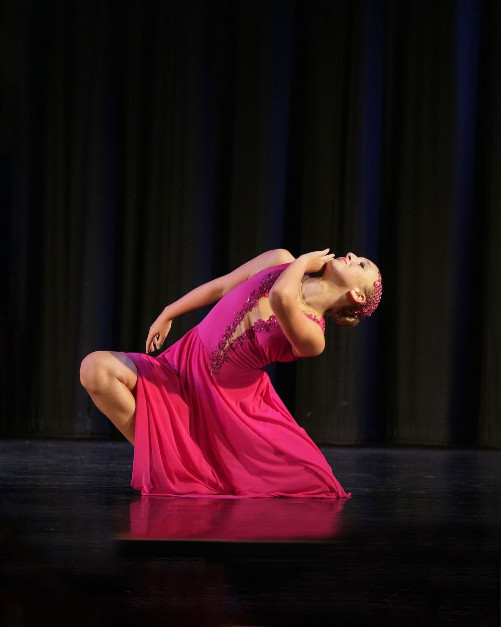 A dancer in a pink dress performs an expressive backbend on stage under dramatic lighting.