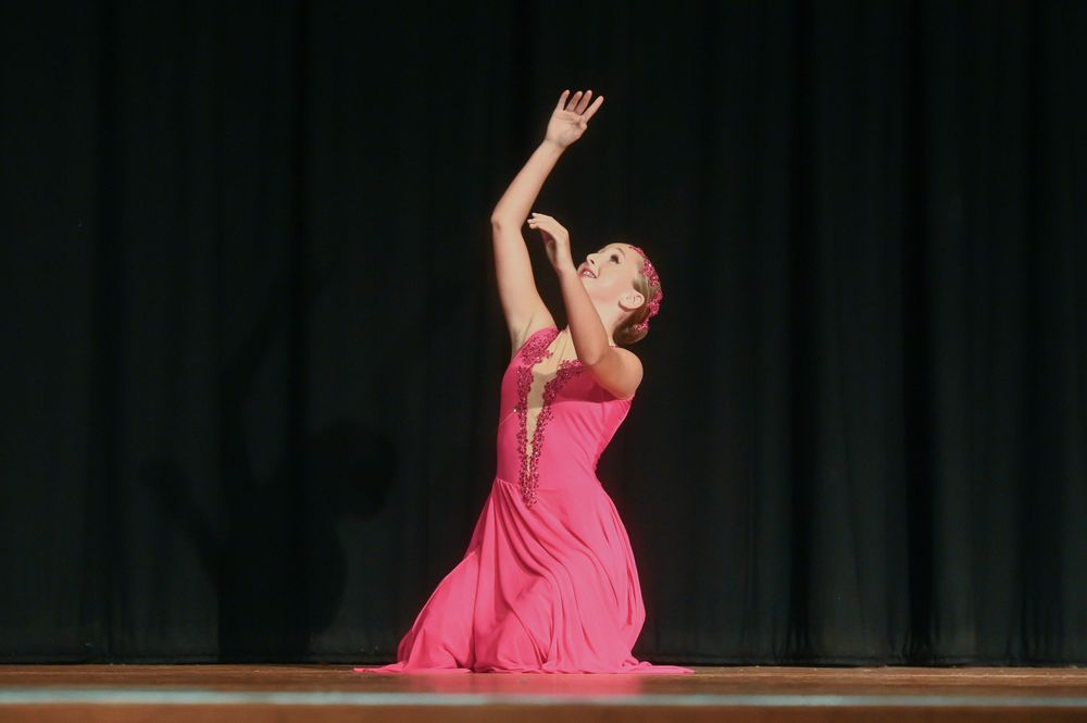 Ballet dancer in pink dress performs elegant leaping movement sequence across dark stage during performance.