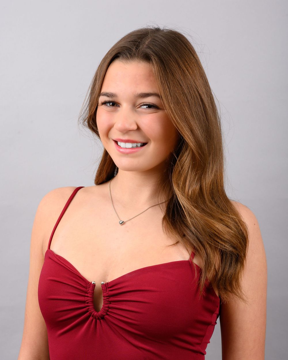 A young woman in a burgundy sleeveless top smiles warmly in a studio portrait photoshoot series.