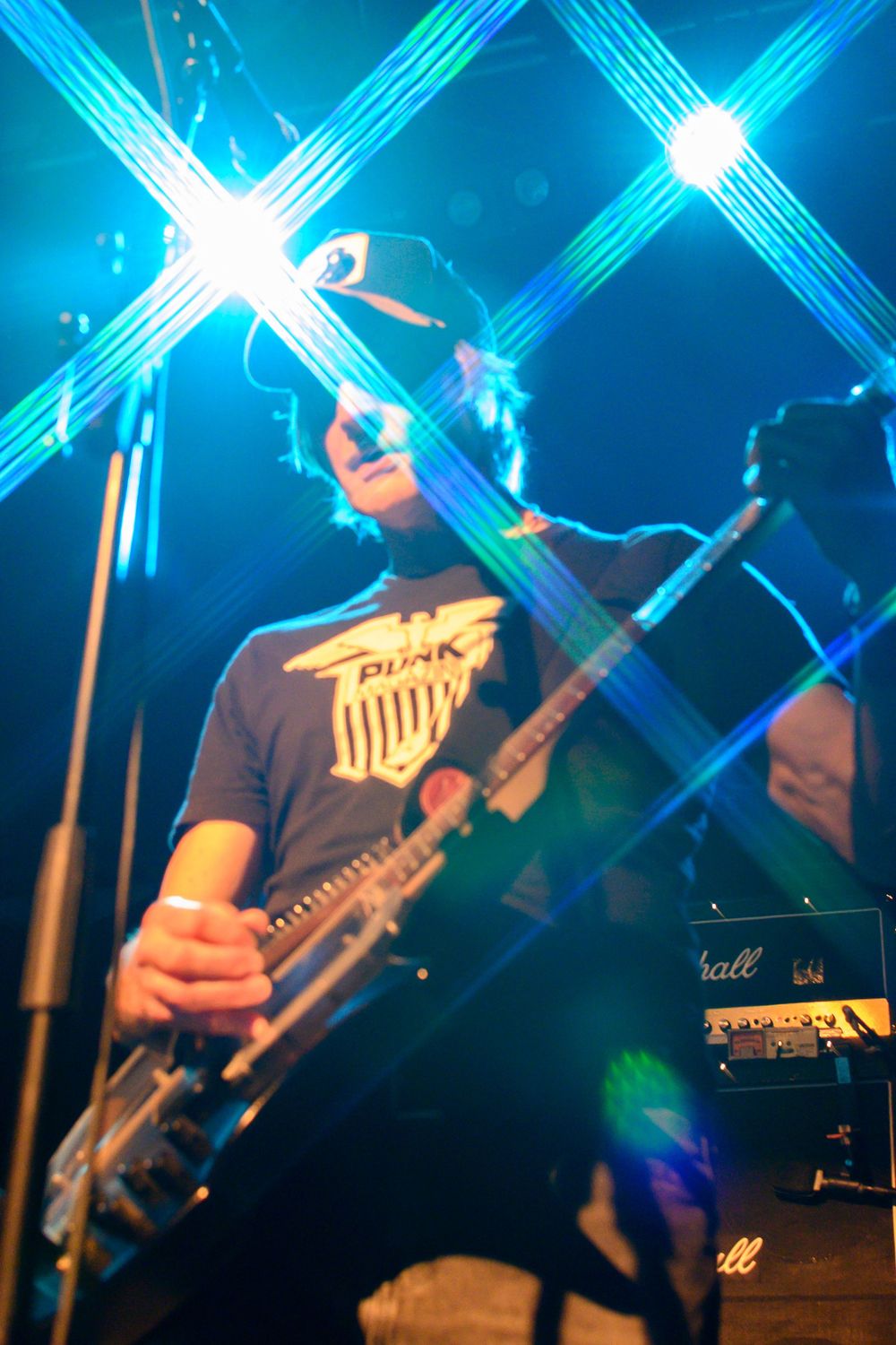 Musicians perform on stage with blue laser light beams creating dramatic X patterns in the dark concert atmosphere.