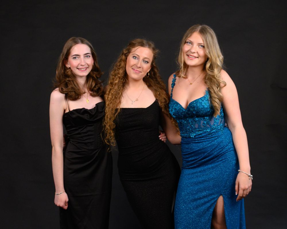 Three people in formal attire stand against a black background with one wearing a striking blue gown.