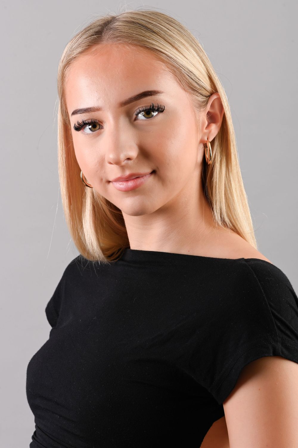 Headshot portrait of a young blonde woman in a black top posing against a gray background.