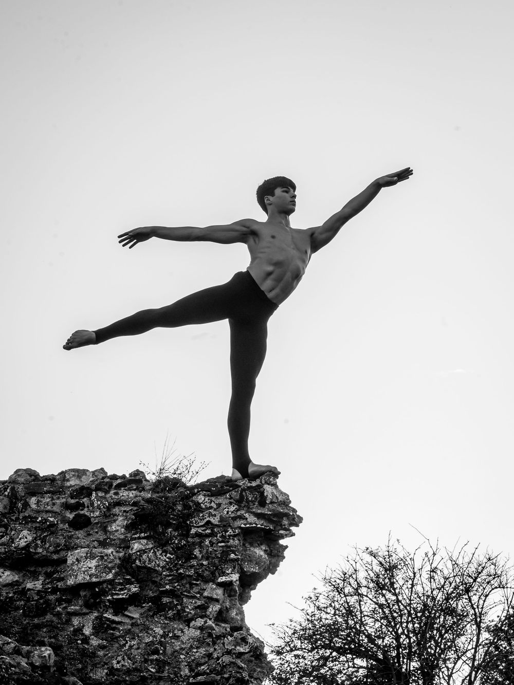 Silhouetted figure performs graceful dance poses on rocky cliff edge against dramatic sky.