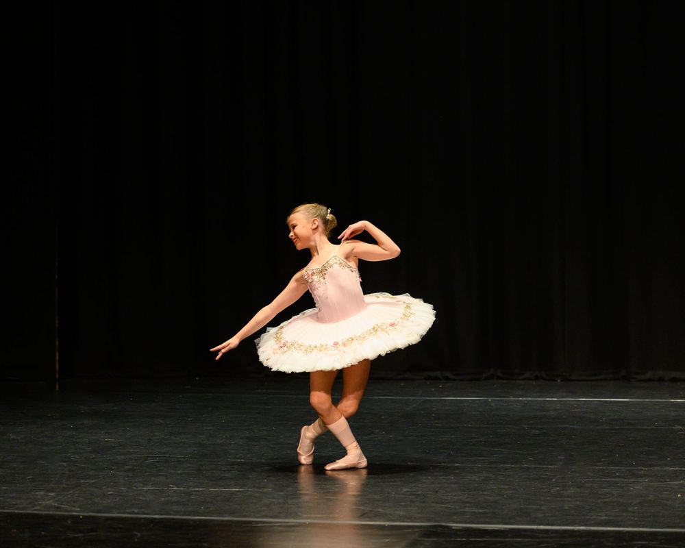 A ballet dancer in a white tutu performs a graceful turn on stage during a solo performance against a dark backdrop.