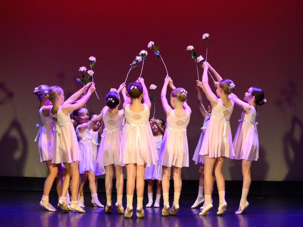 Ballet dancers in white dresses perform synchronized movements in line formation under dramatic stage lighting.