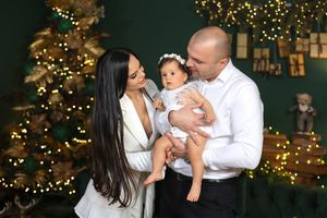Family Christmas portrait in front of decorated tree with bokeh lights and wrapped presents.
