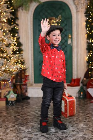 Child in red shirt and black pants plays near decorated Christmas tree and wrapped presents.