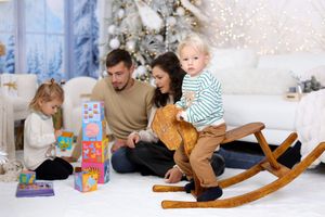 Family holiday scene with wooden rocking horse and toys in snowy white Christmas setting.