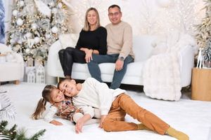 Cozy winter family portrait with white Christmas trees and snowy decorations in background.