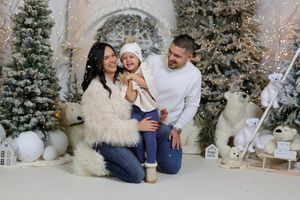 Family of three posing in a festive Christmas photo studio with snowy trees, polar bears, and holiday decorations.