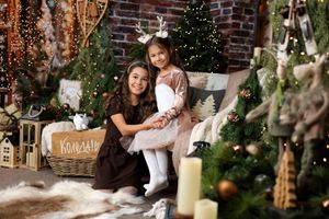 Woman and girl in reindeer antlers pose together by decorated Christmas trees with lights and candles.